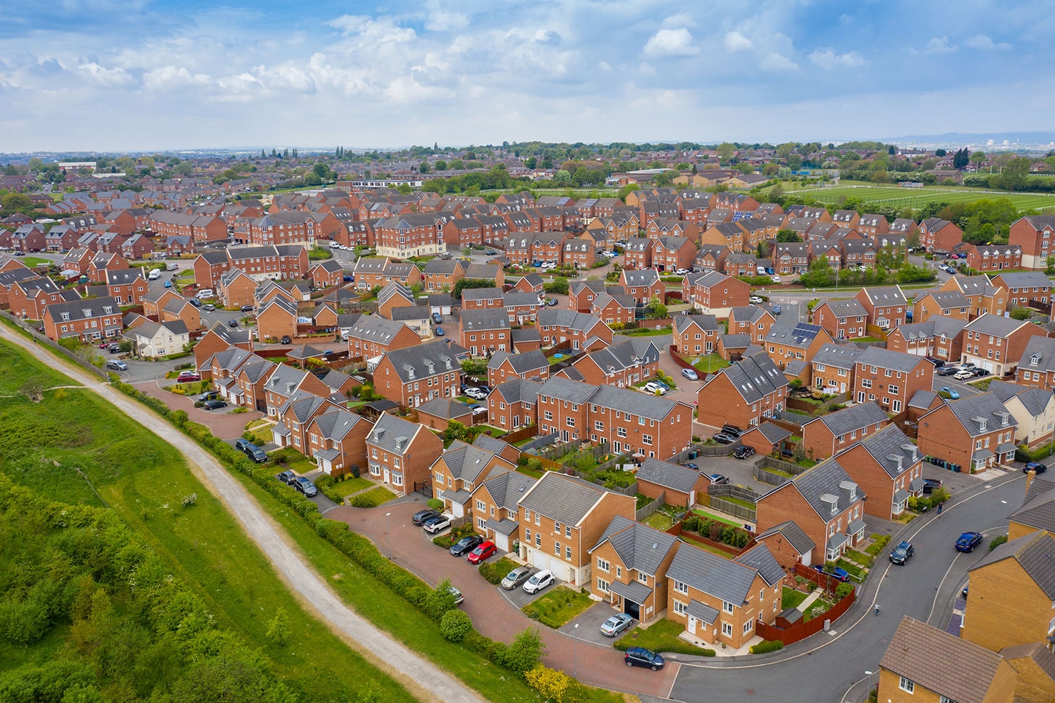Aerial view of a large suburban housing estate with rows of red-brick homes and green spaces.